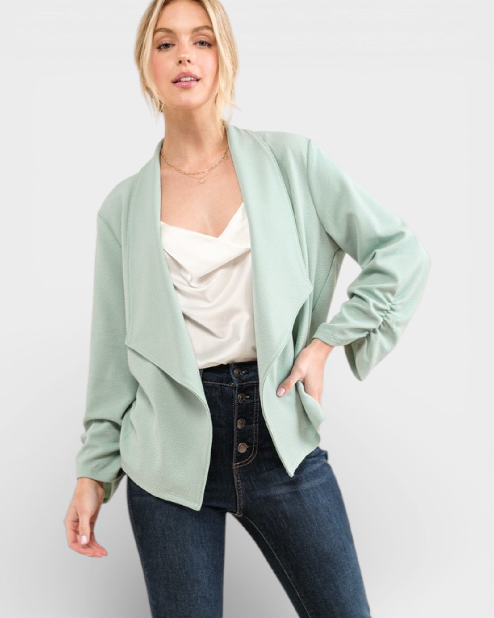 Woman wearing a light green blazer over a white top and blue jeans on a white background