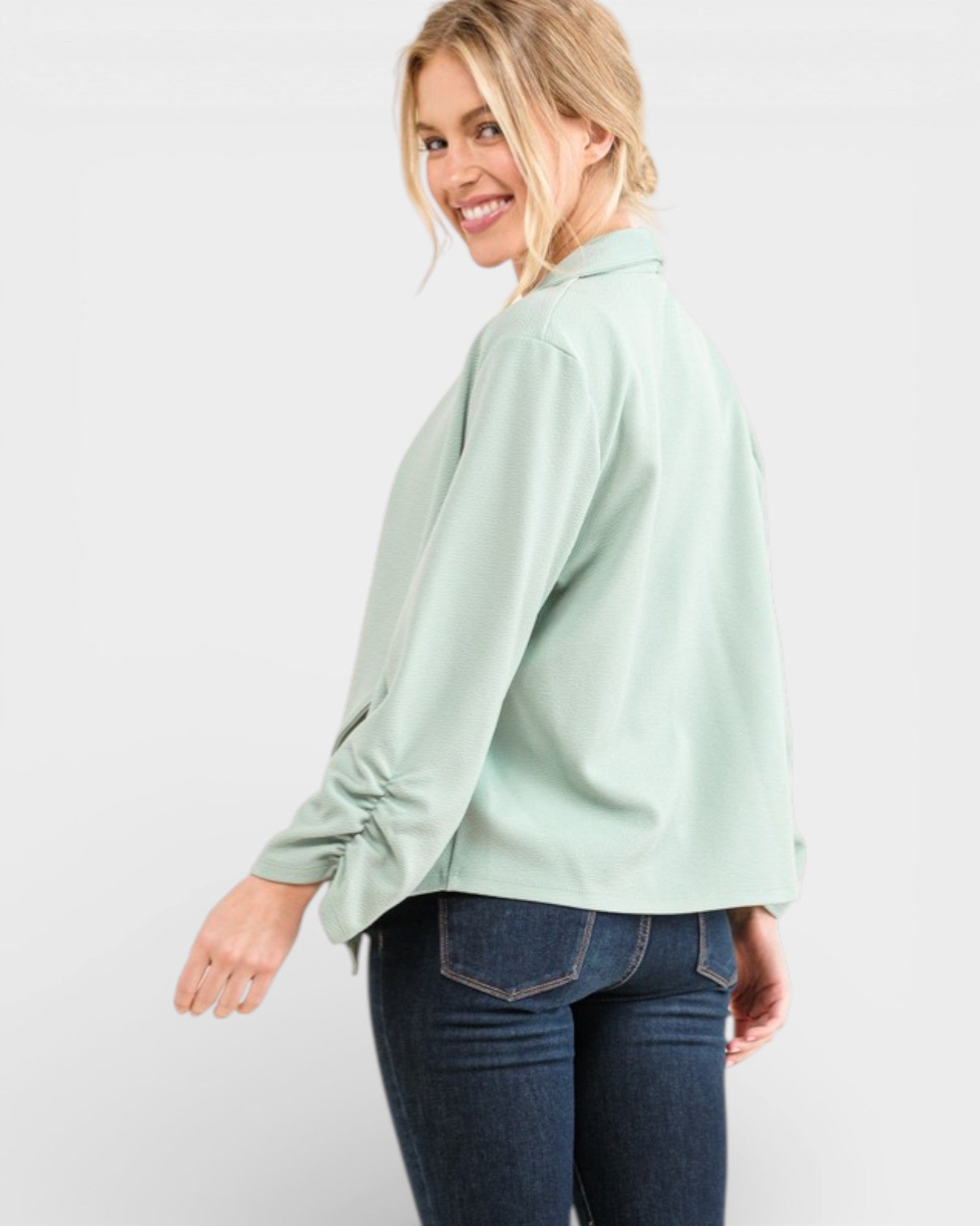 Woman wearing a light green blouse and blue jeans on a white background