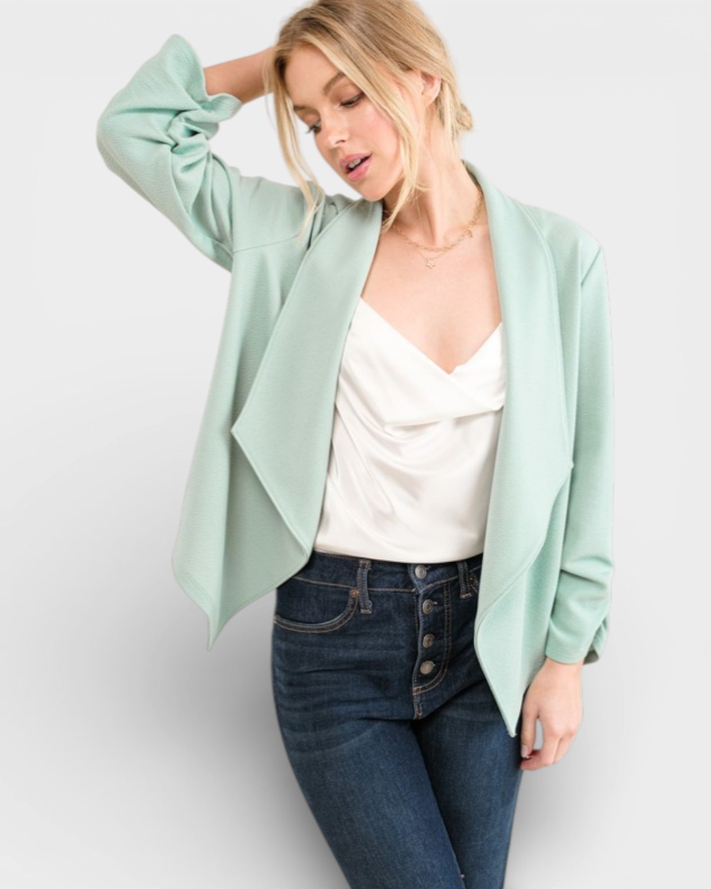 Woman wearing a light green blazer over a white top and blue jeans on a white background