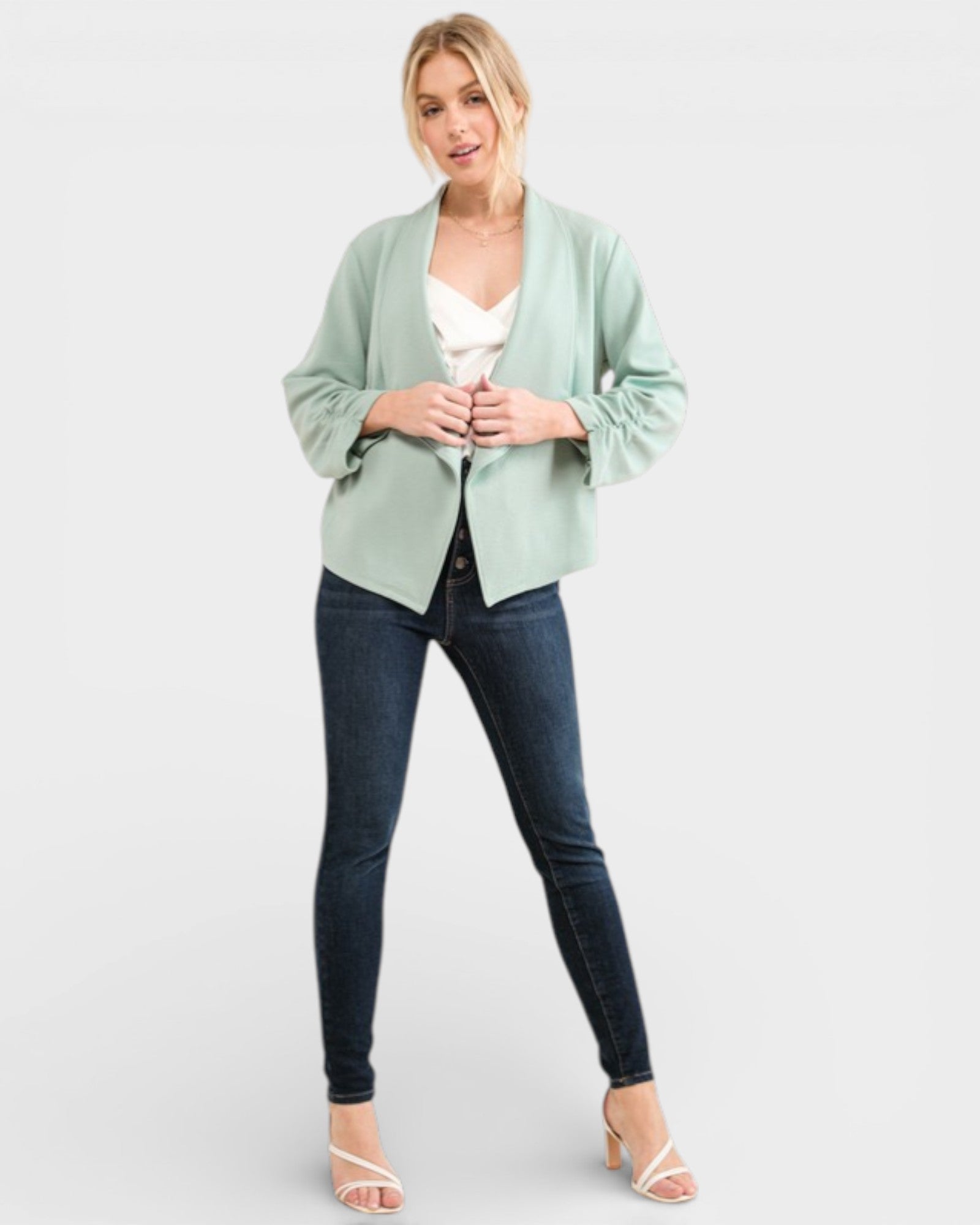 Woman wearing a light green cardigan, white top, and dark jeans on a white background