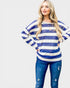 Woman wearing a blue and white striped sweater with blue jeans on a plain background