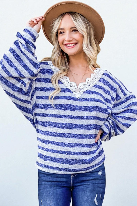 Woman wearing a blue and white striped sweater with lace details, blue jeans, and a brown hat on a light background.