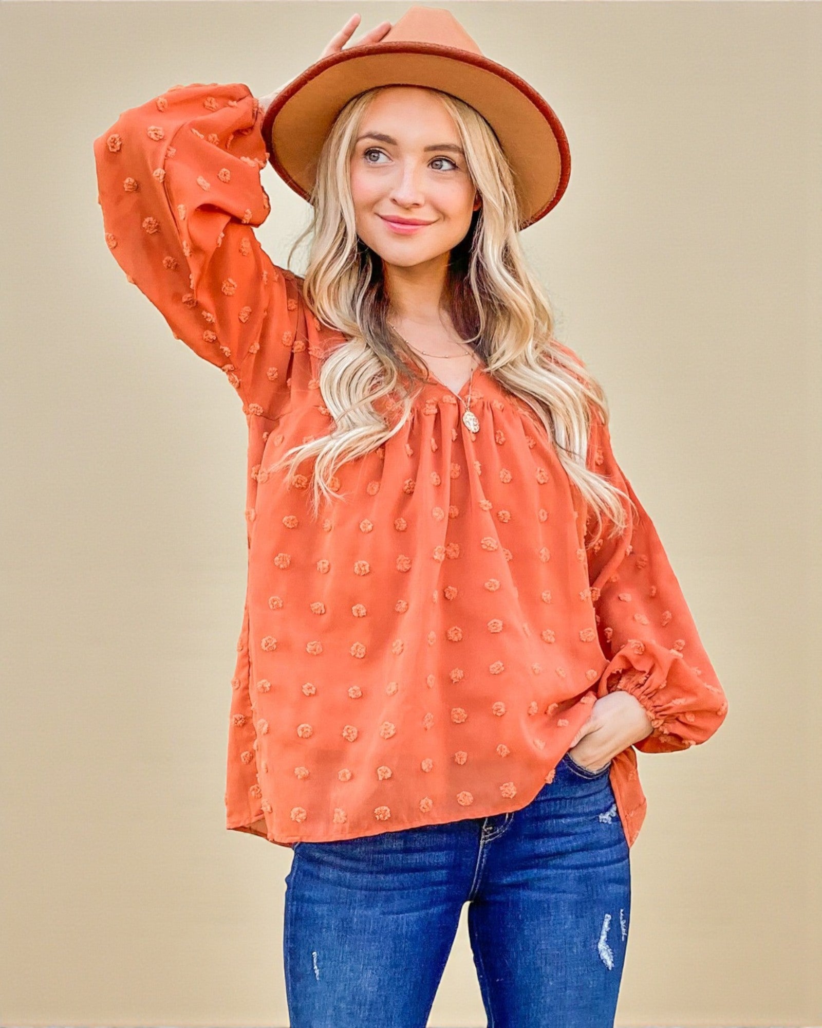 Woman wearing an orange polka dot blouse and blue jeans against a beige background
