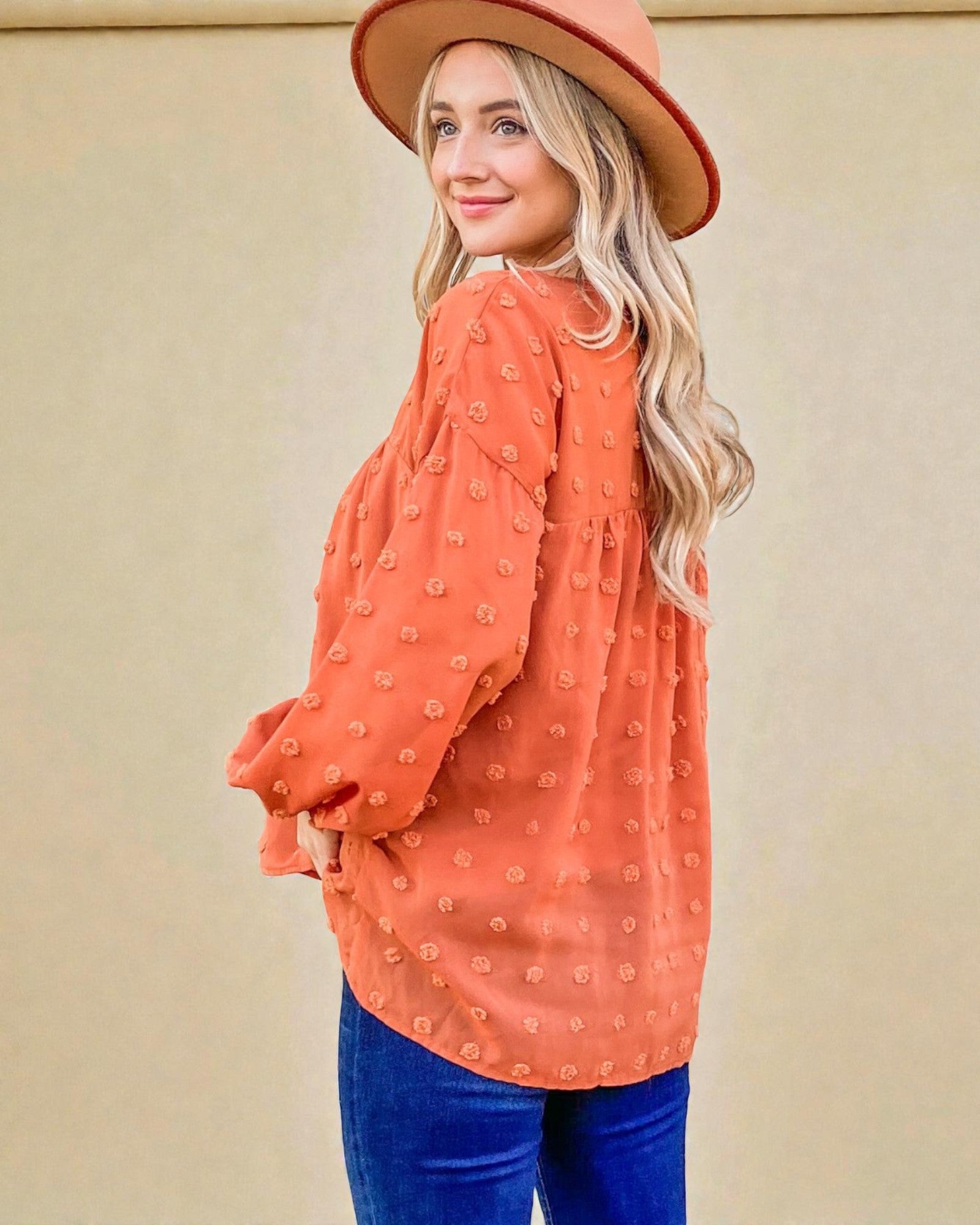 Woman wearing an orange polka dot blouse and blue jeans with a beige background