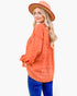 A woman wearing a terracotta orange textured long-sleeve blouse, blue jeans, and a matching terracotta hat, photographed against a solid white background.