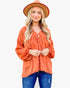 A woman wearing a burnt orange long-sleeve blouse with a textured dot pattern, blue jeans, and a matching burnt orange wide-brim hat, photographed against a solid white background.