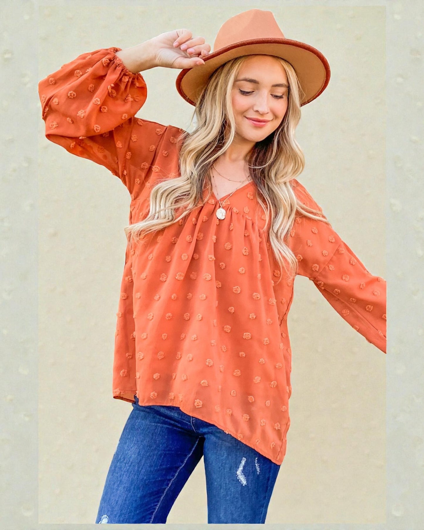 Woman wearing an orange patterned blouse and blue jeans with a beige background