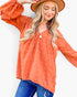 A woman wearing a terracotta orange long-sleeve blouse with a textured, raised dot pattern, paired with blue jeans and a brown wide-brim hat, set against a plain white background.