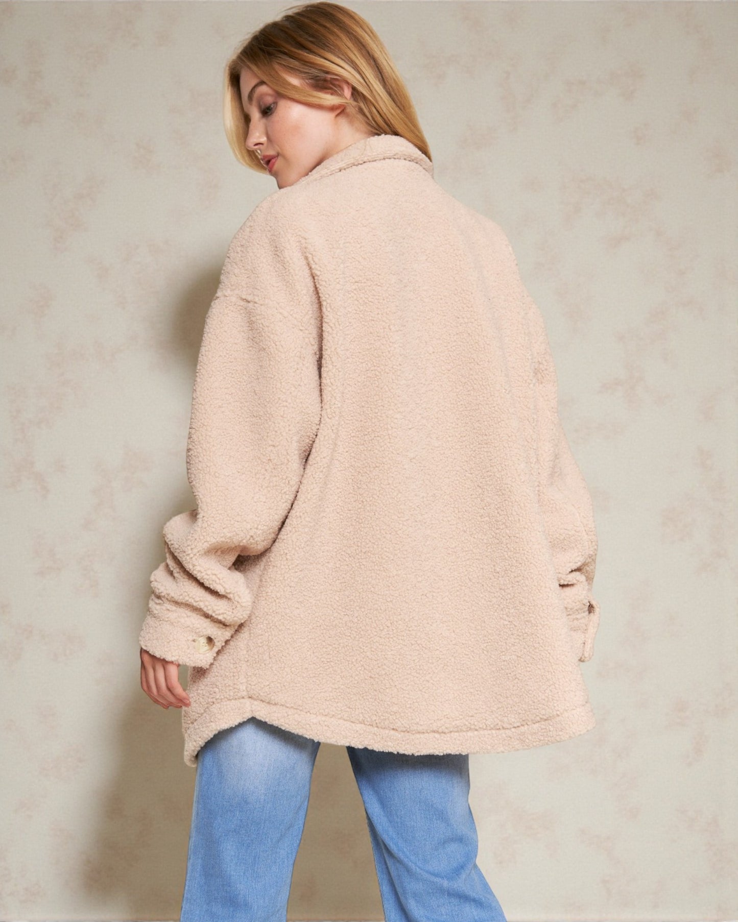 Woman wearing a beige coat and blue jeans against a plain background