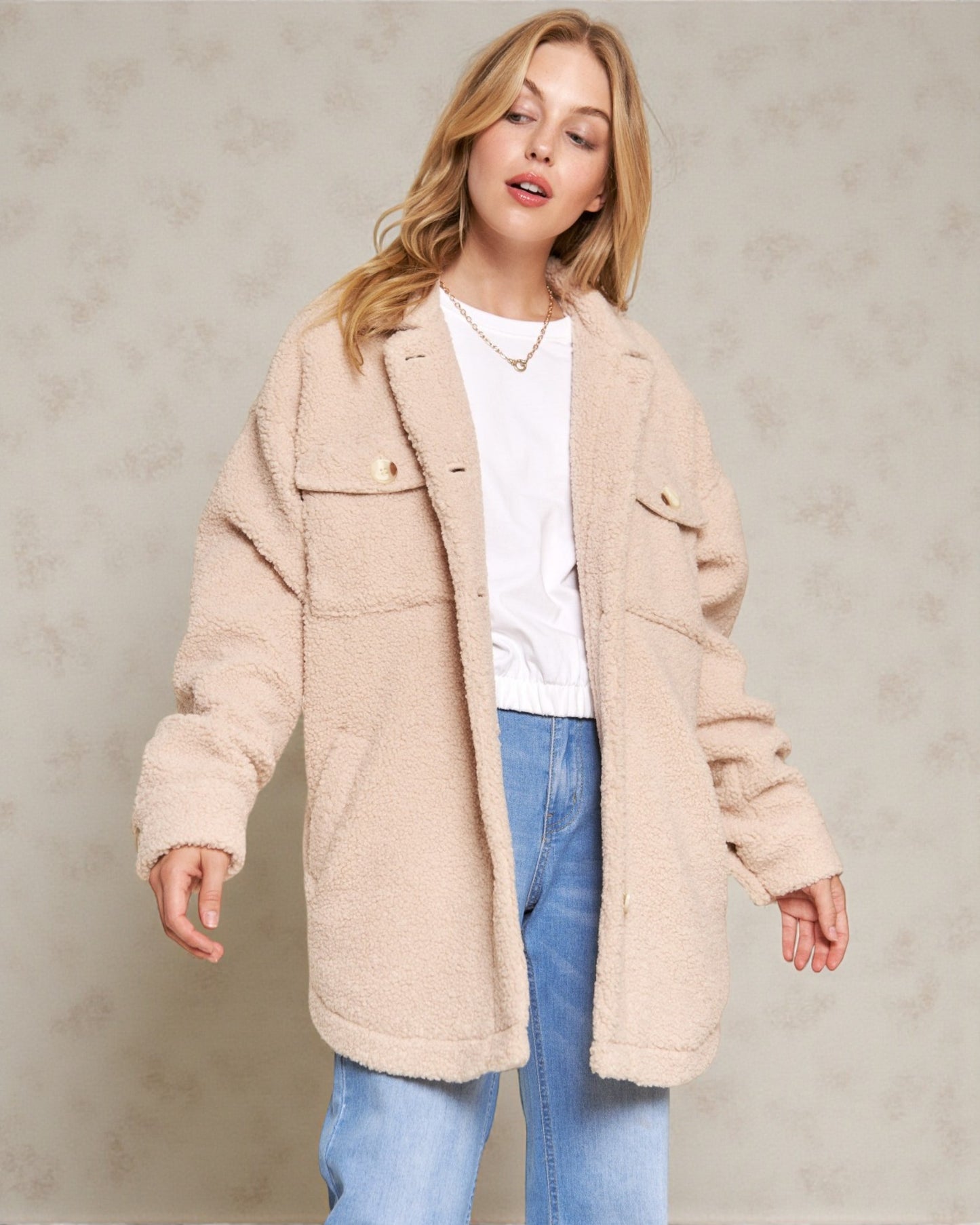 Woman wearing a beige coat and blue jeans against a neutral background