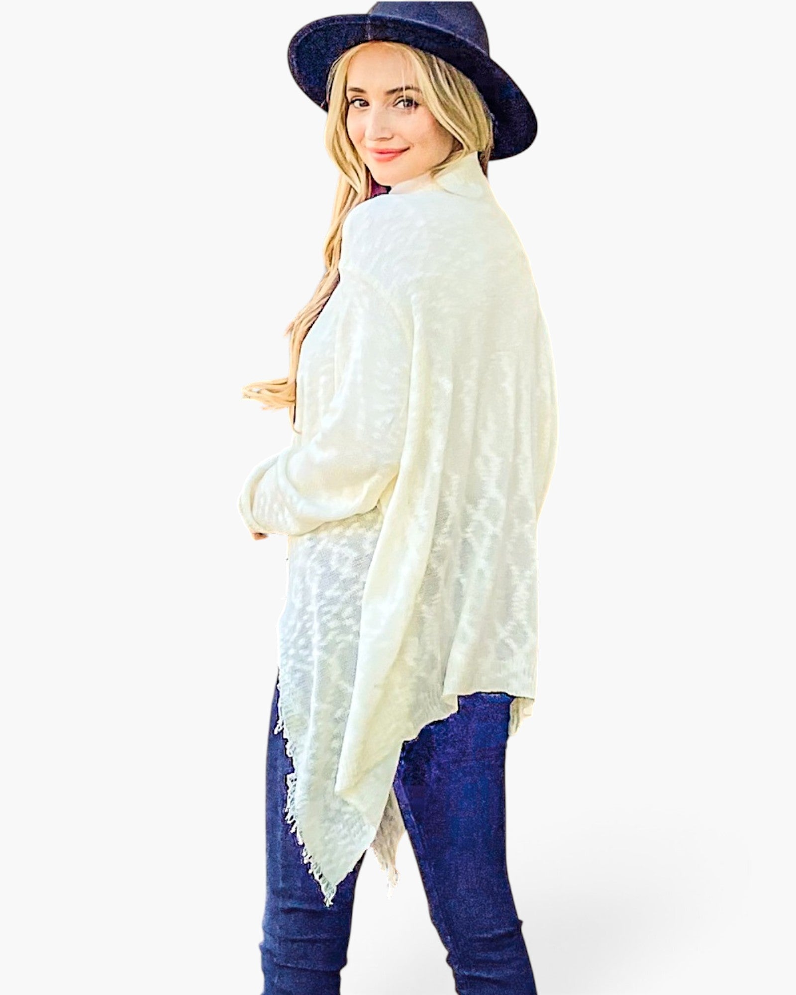 A woman wearing a cream-colored lace-trimmed shawl poncho over a purple top, paired with blue jeans and a navy blue wide-brim hat, photographed against a solid white background.