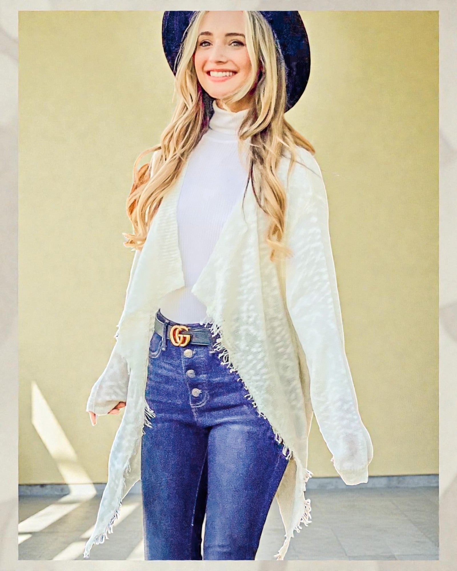 Woman wearing a white cardigan, white top, and blue jeans with a yellow background