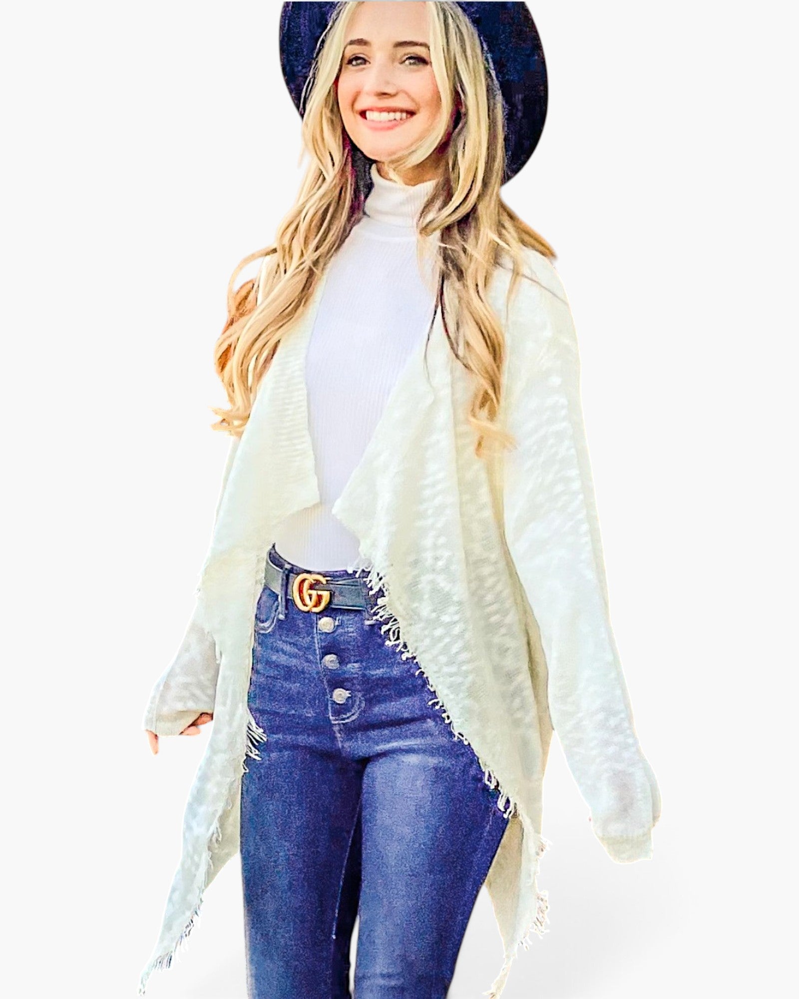 A woman modeling a long, open-front cream knit cardigan with frayed edges, worn over a white turtleneck and blue jeans with a Gucci belt, against a plain white background.