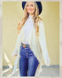 Woman wearing a white cardigan, white top, and blue jeans with a yellow background