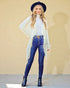 Woman wearing a white lace cardigan, blue jeans, and black boots against a beige wall.