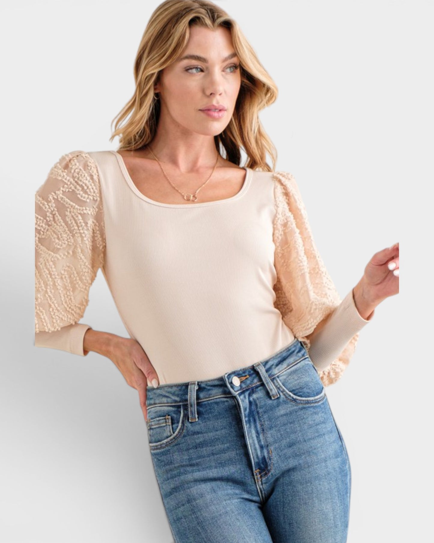 Woman wearing a beige top with lace sleeves and blue jeans on a white background