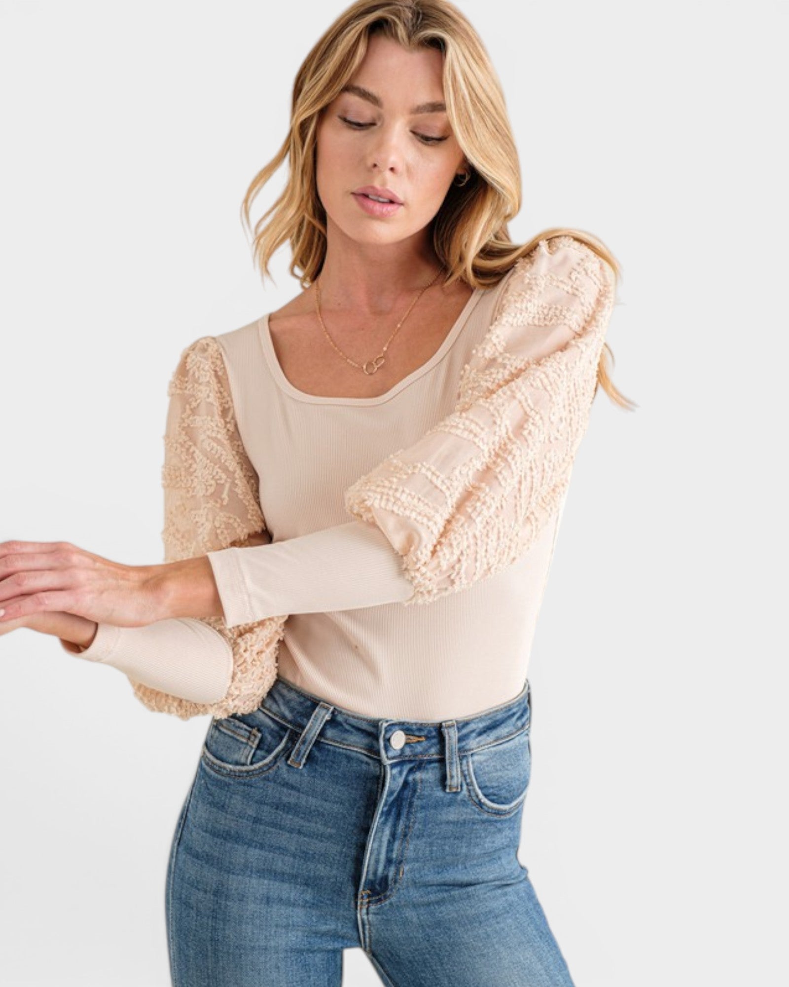 Woman wearing a beige knit cardigan over a cream top and blue jeans on a white background