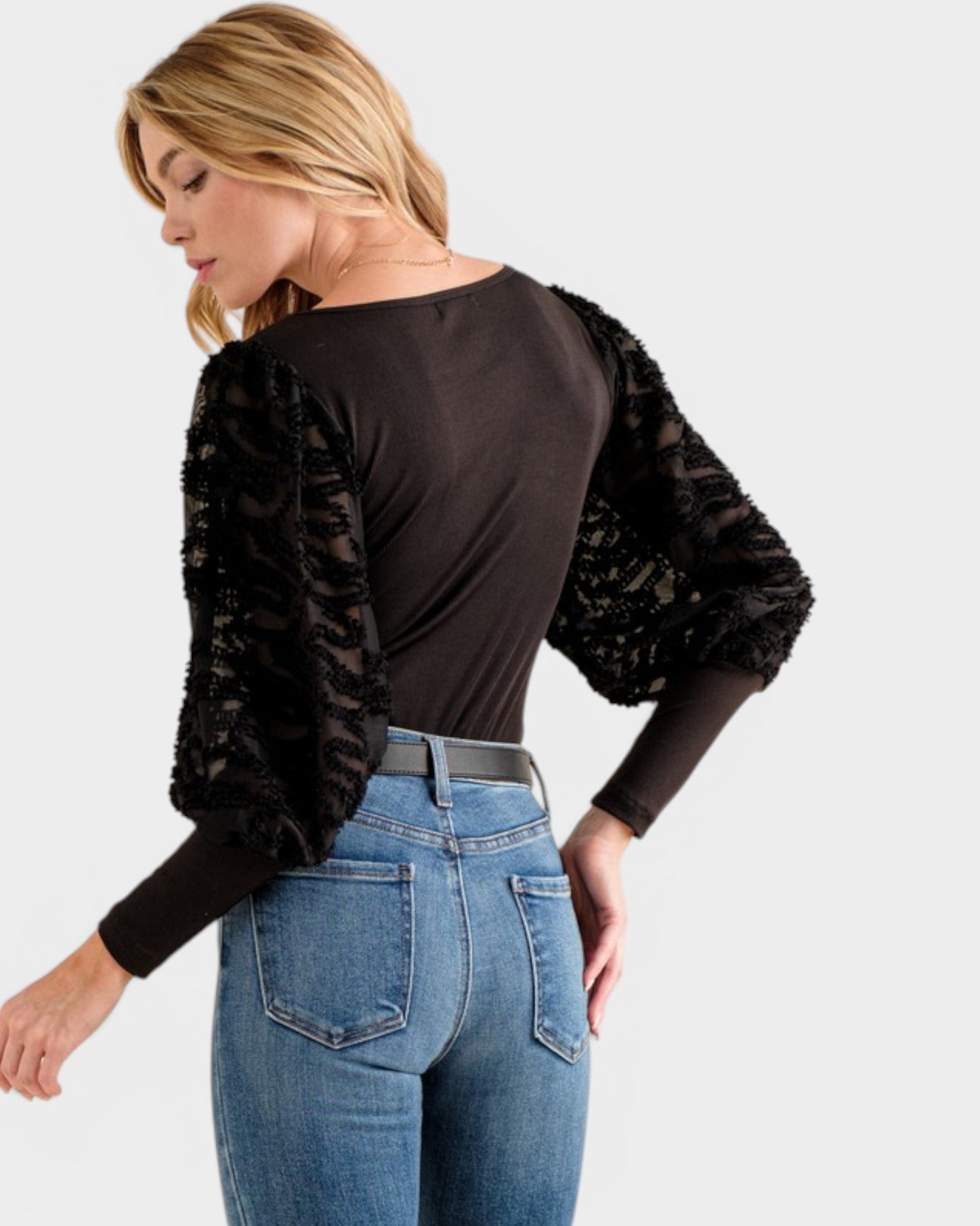 Woman wearing a black long-sleeve top with sequin sleeves and blue jeans on a white background