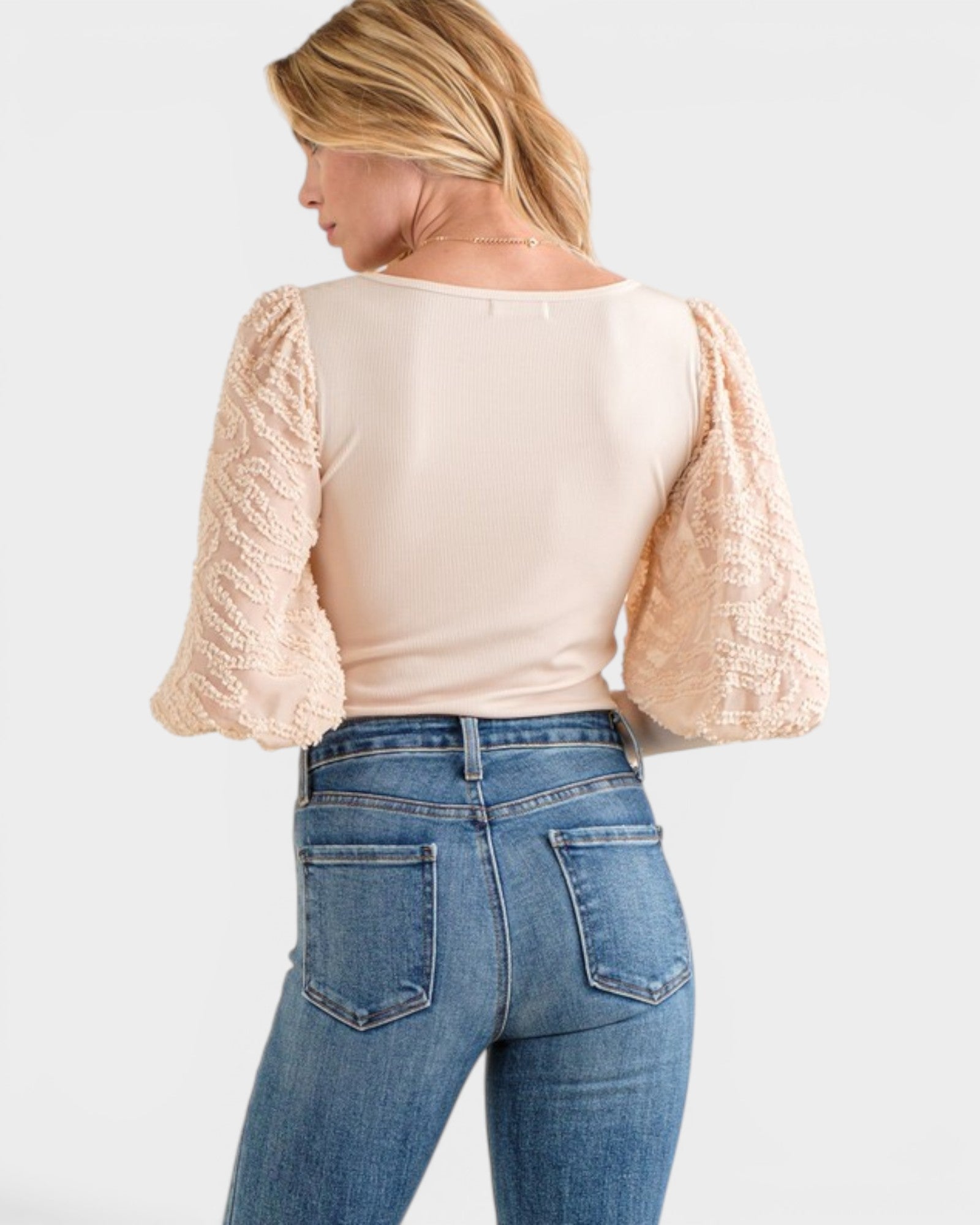 Woman wearing a beige top with ruffled sleeves and blue jeans on a white background