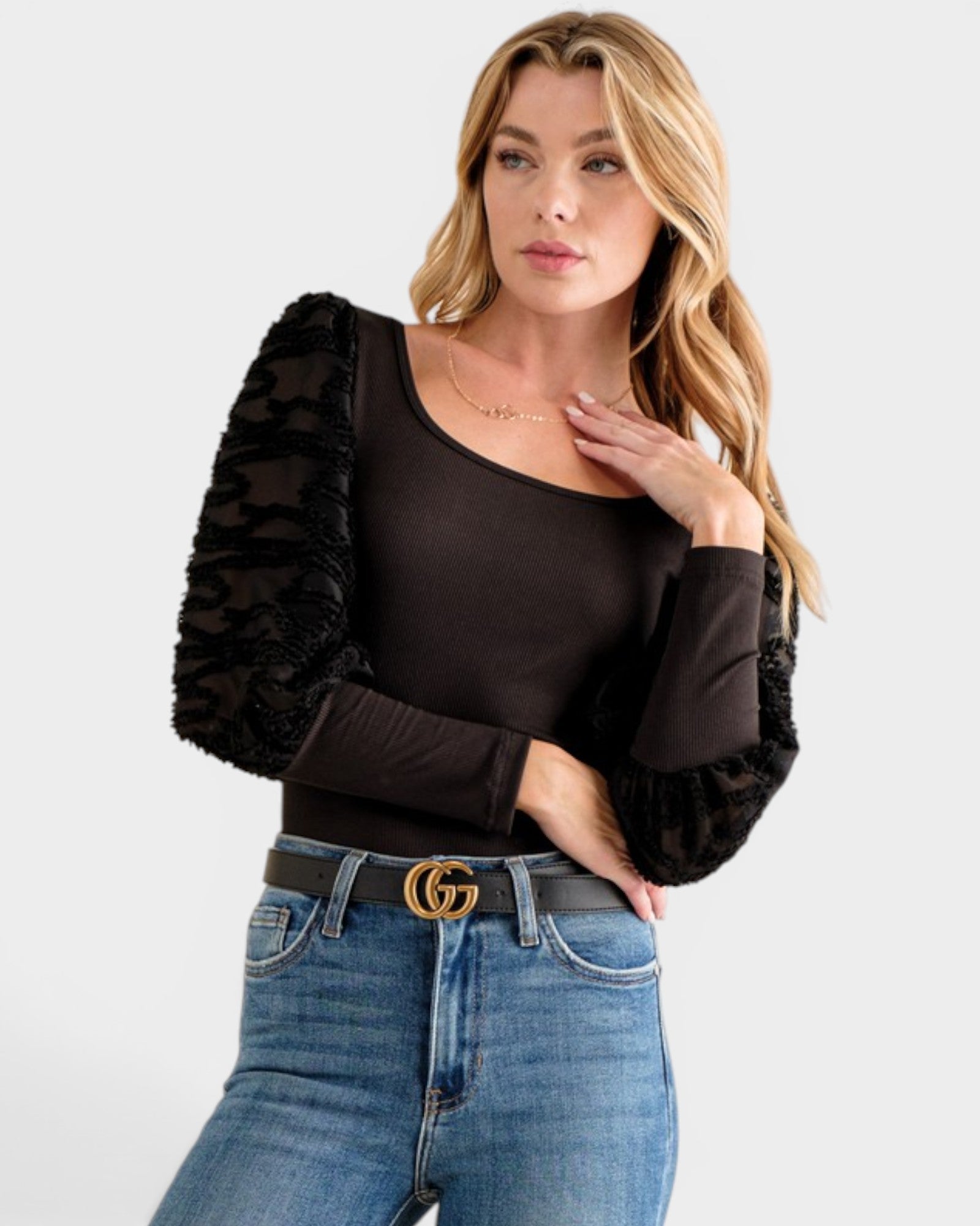 Woman wearing a black top with sheer sleeves and blue jeans on a white background