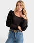 Woman wearing a black top with sheer sleeves and blue jeans on a white background