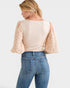 Woman wearing a beige top with ruffled sleeves and blue jeans on a white background