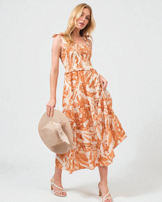 Woman wearing an orange and white patterned dress holding a hat on a white background