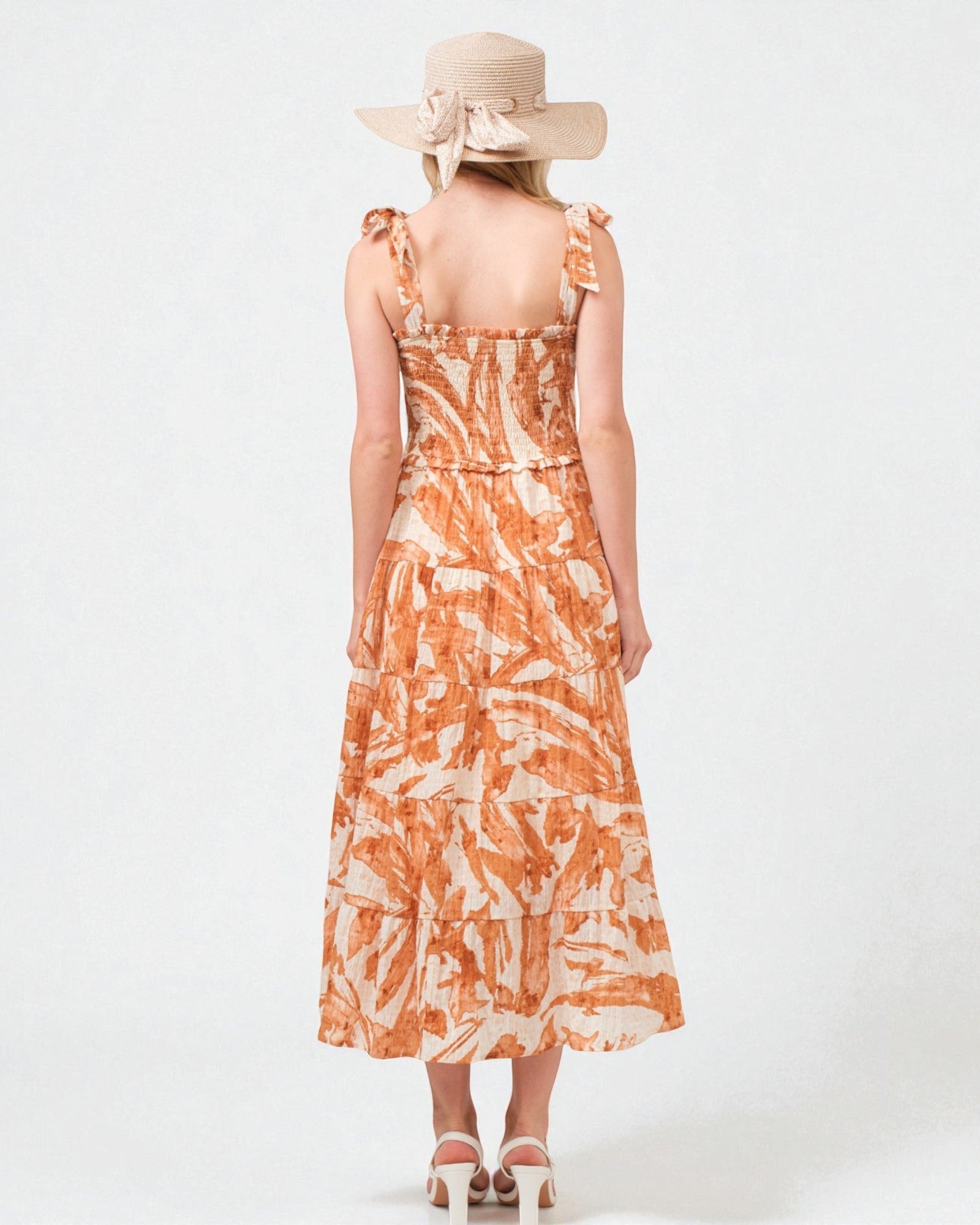 Woman wearing an orange and white patterned dress with a wide-brimmed hat on a white background
