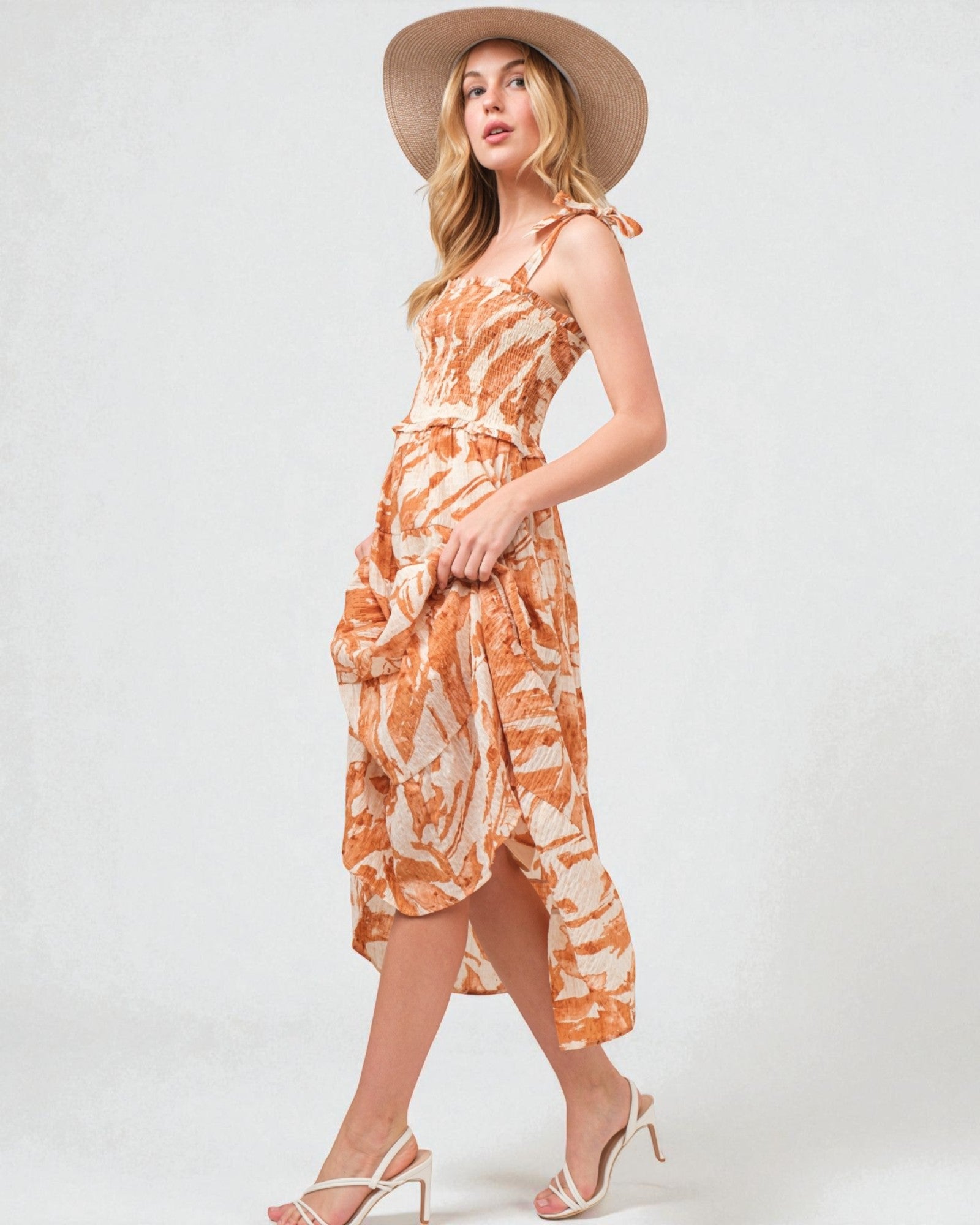 Woman wearing an orange and white patterned dress with a straw hat on a white background