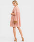 Woman wearing a pink dress holding a woven bag on a light gray background