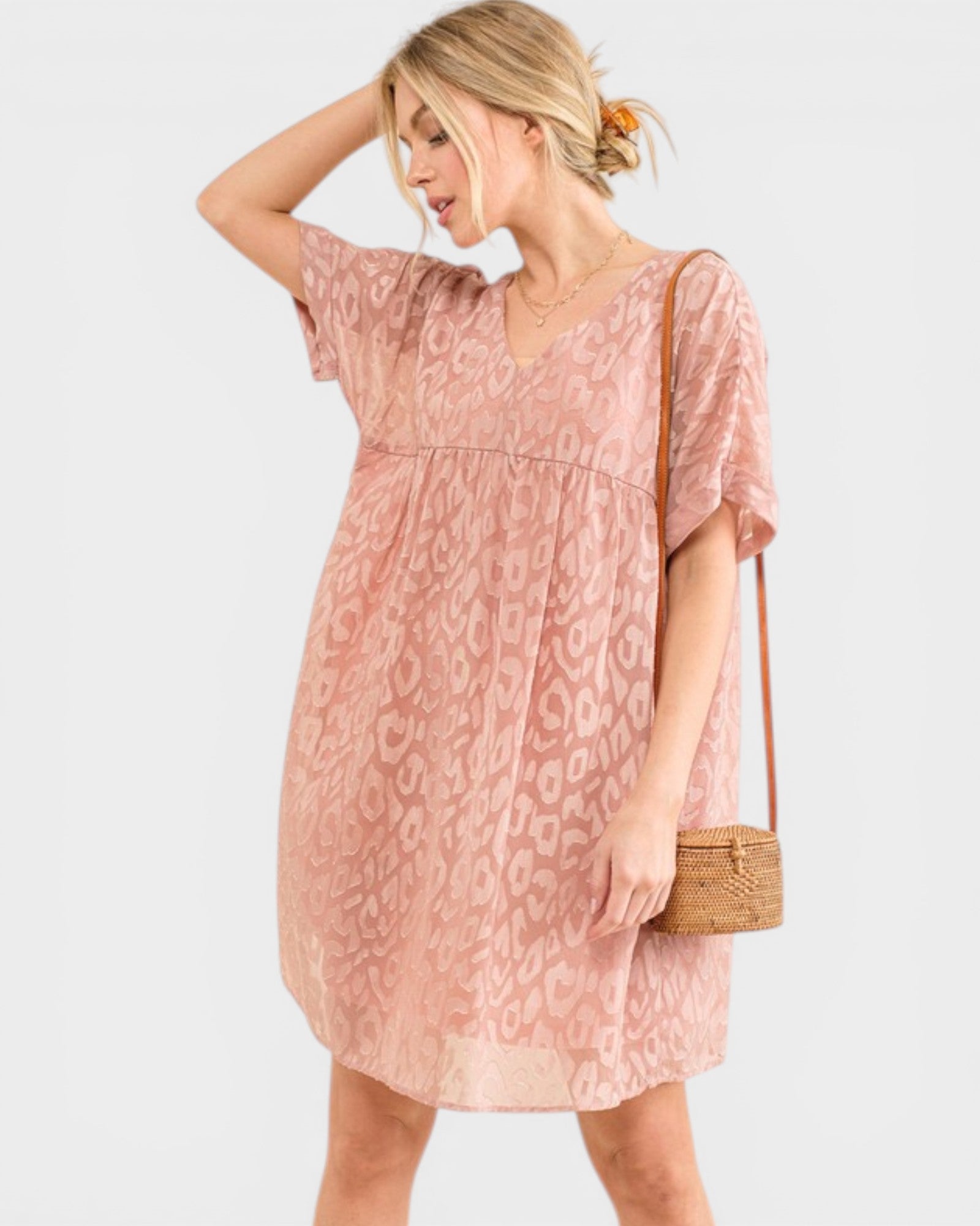 Woman wearing a pink patterned dress holding a small bag on a white background