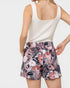 Person wearing a white tank top and floral shorts on a plain background