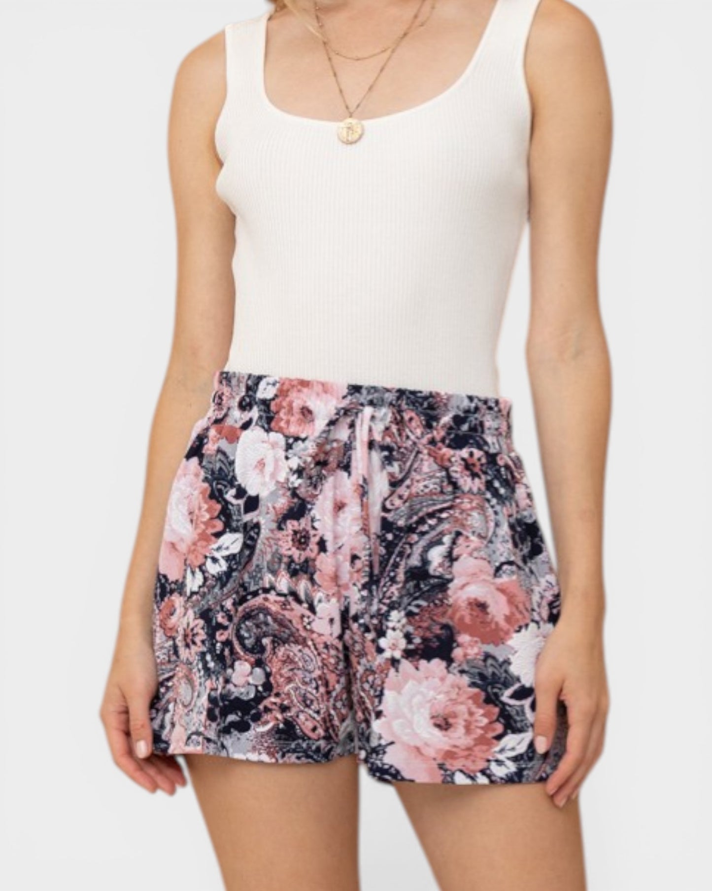 Person wearing a white tank top and floral shorts on a plain background