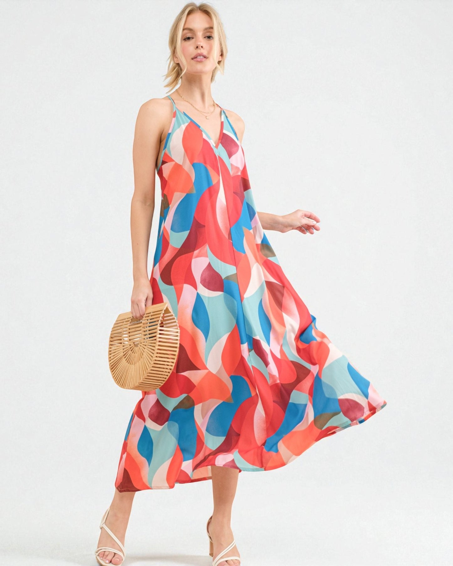 Woman wearing a colorful patterned dress holding a woven bag on a white background