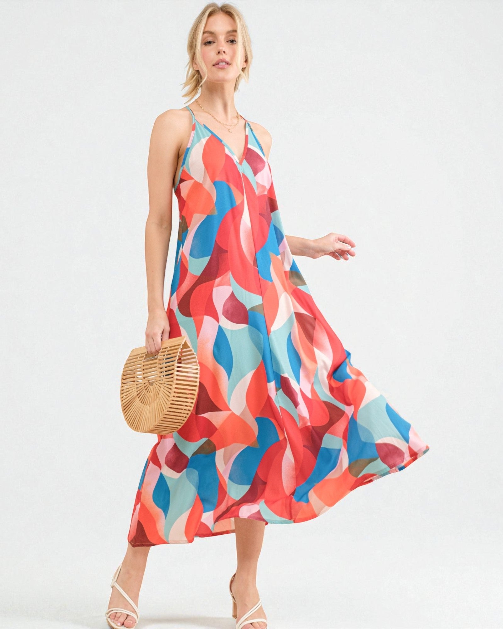 Woman wearing a colorful patterned dress holding a woven bag on a white background