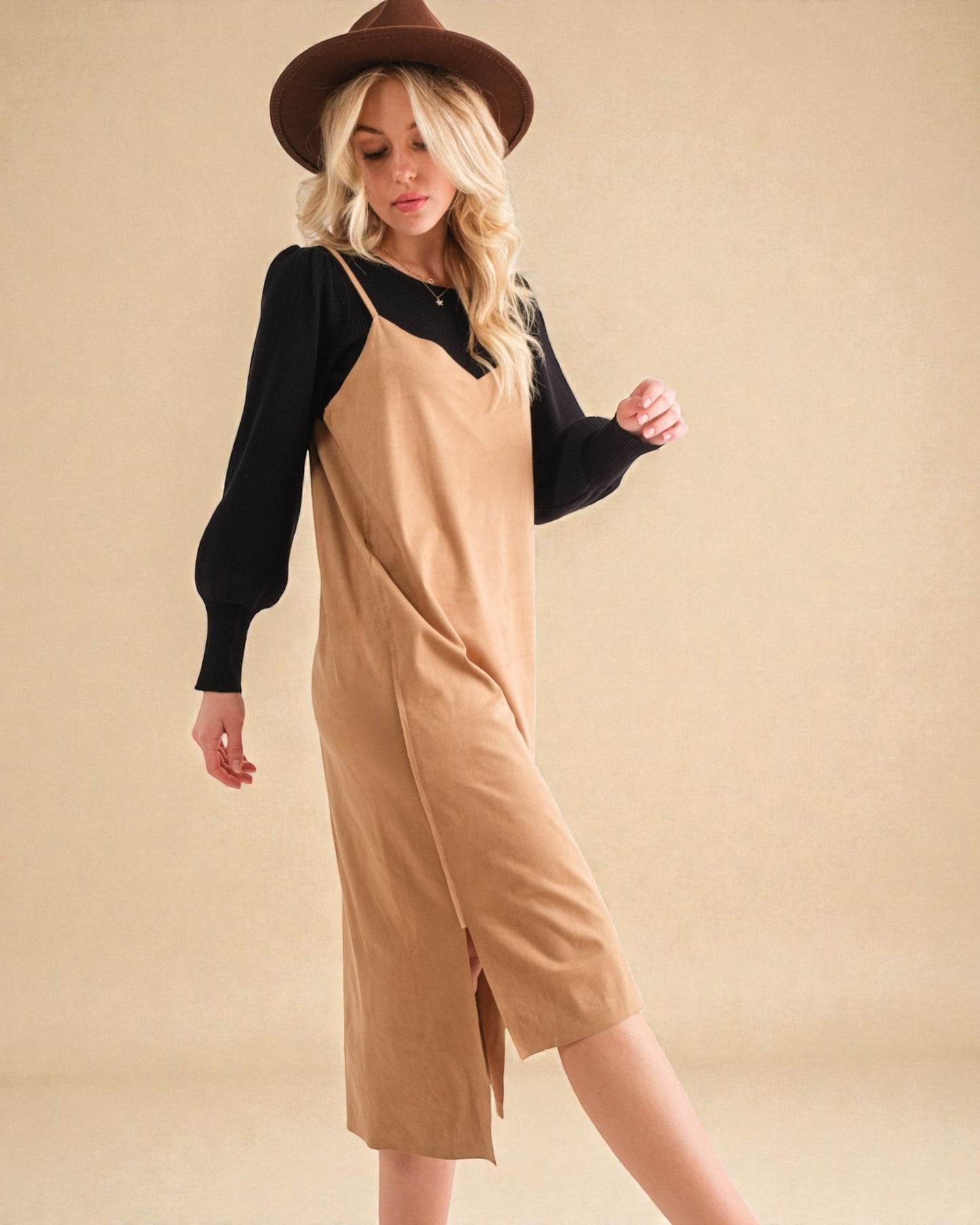 Woman wearing a beige dress with black sleeves and a brown hat on a beige background