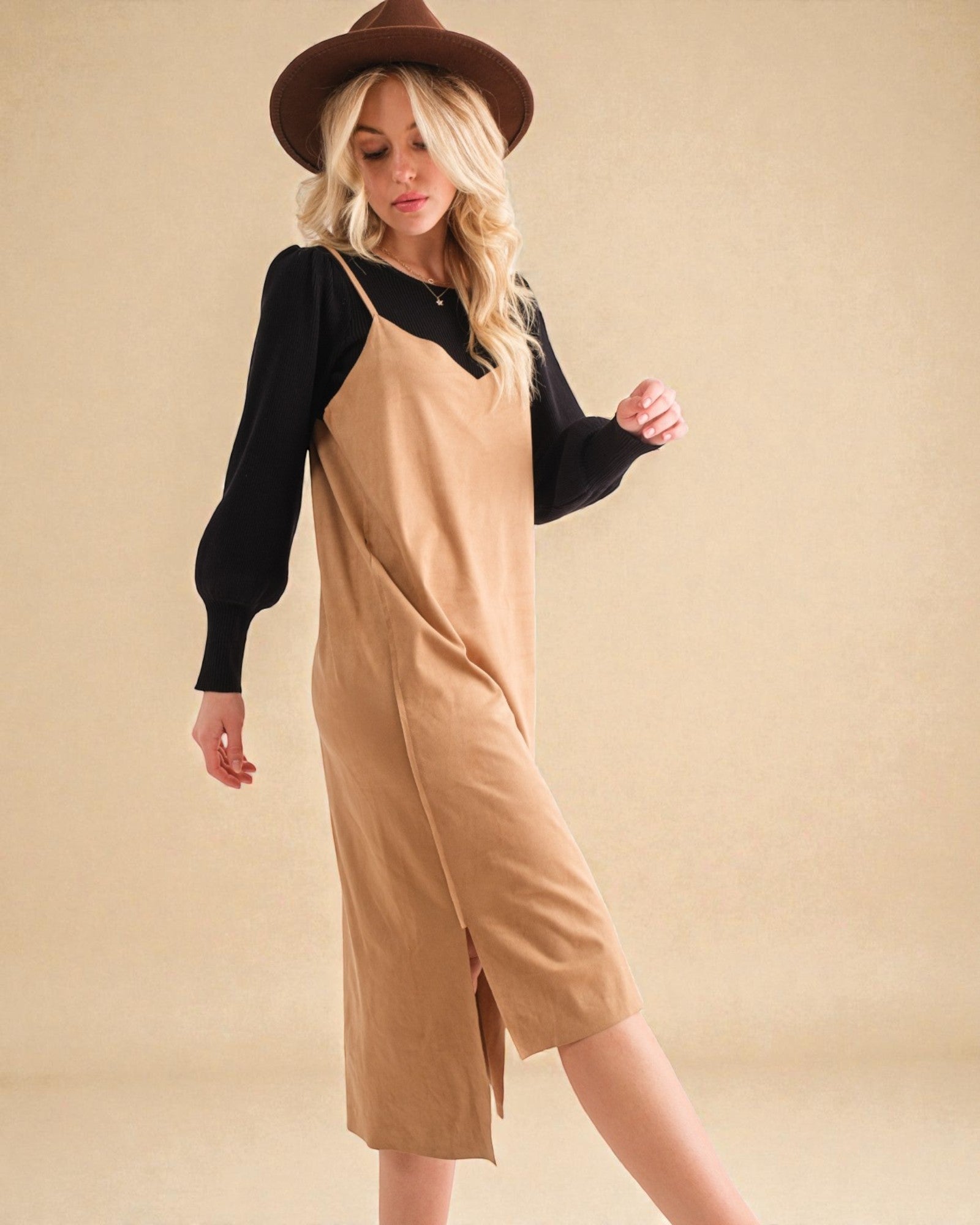 Woman wearing a beige dress with black sleeves and a brown hat on a beige background