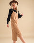 Woman wearing a beige dress with black sleeves and a brown hat on a beige background