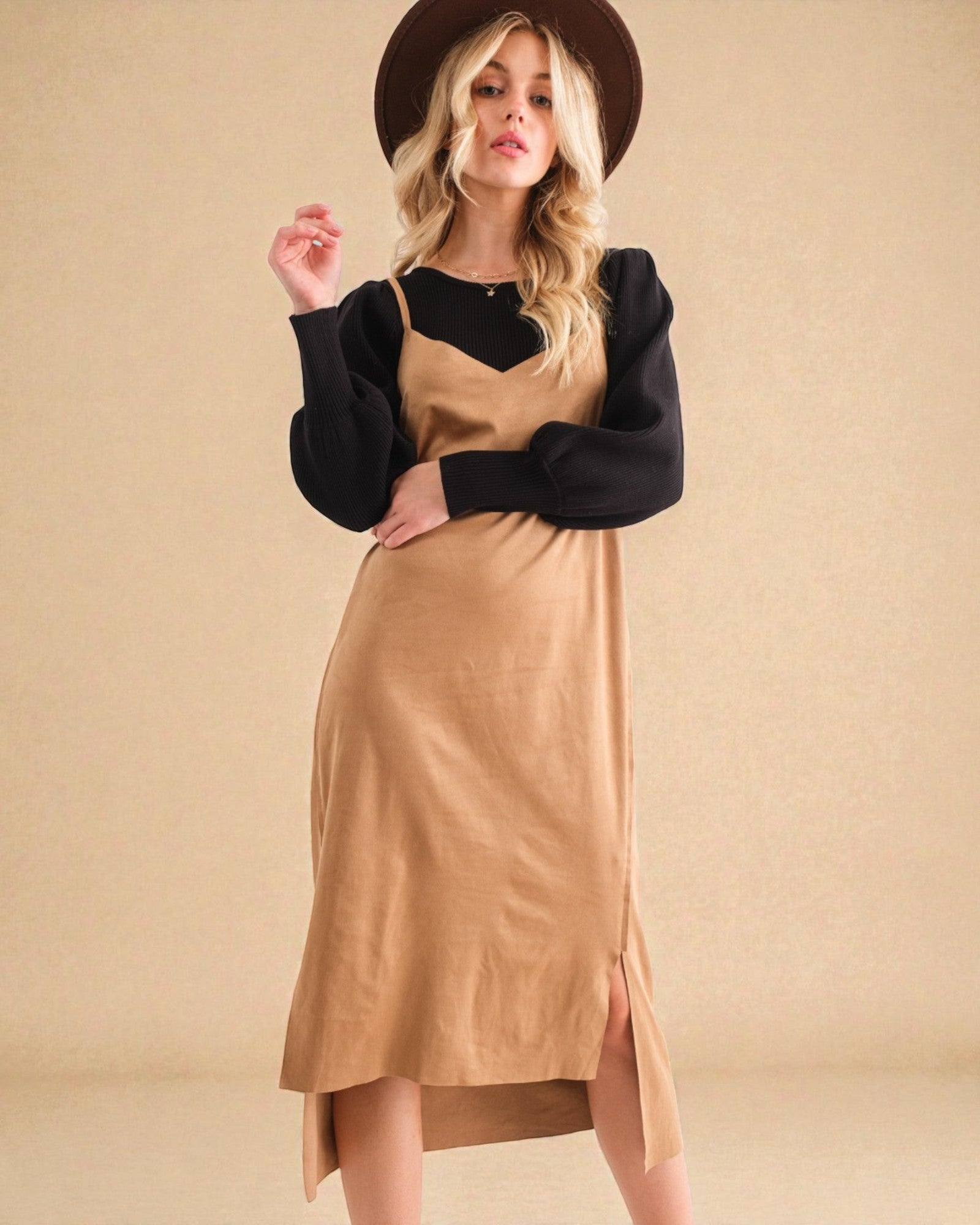 Woman wearing a black sweater with a high-low hem and a beige apron against a beige background