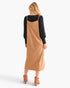 A woman shown from the back wearing a black long-sleeve top under a camel-colored midi slip dress, paired with tan ankle boots, against a light gray studio background.