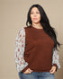 Woman wearing a brown sweater with floral sleeves against a beige background