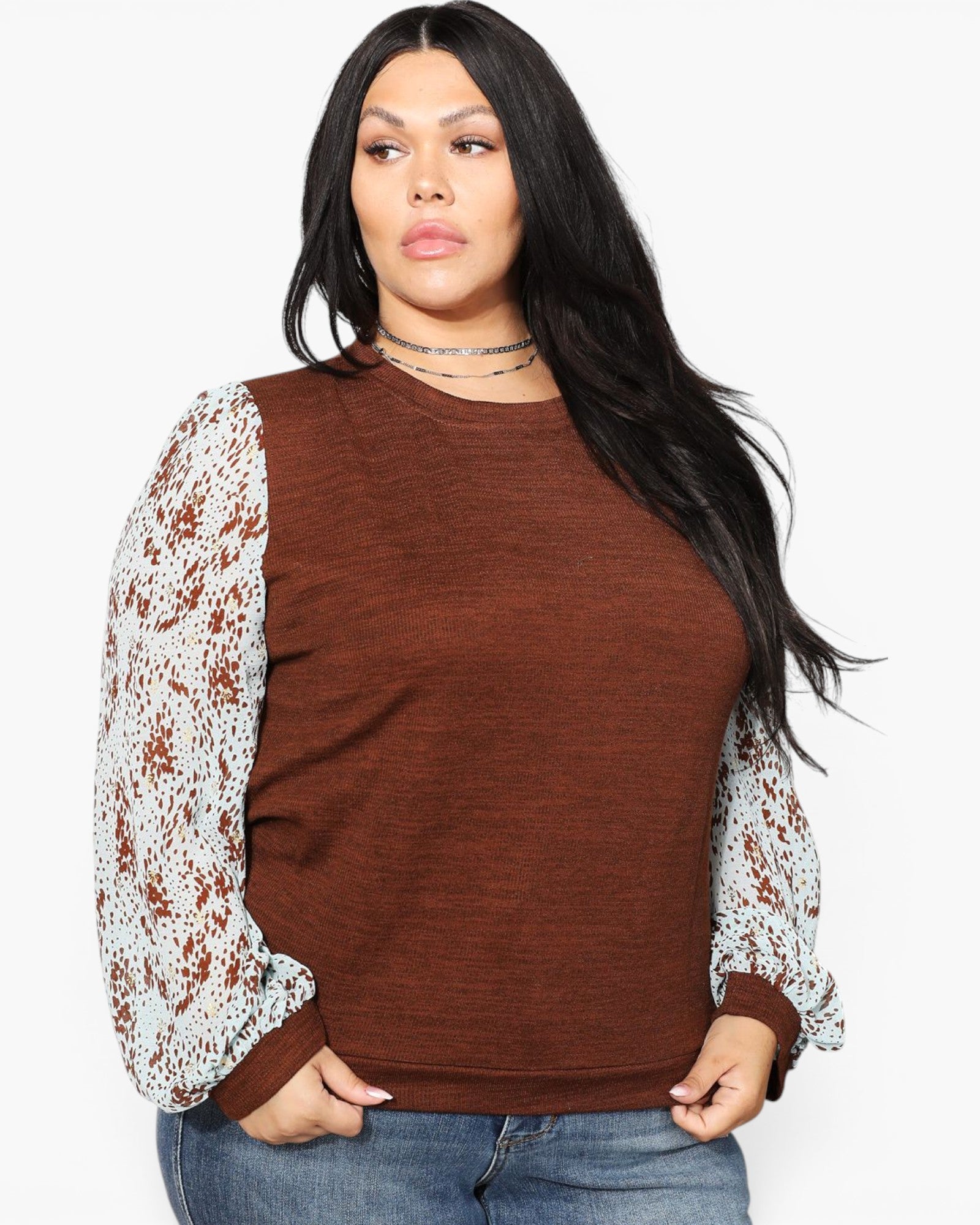 A woman modeling a brown crewneck sweater with long white lace sleeves, paired with blue jeans, against a plain white background.