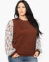 A woman modeling a brown crewneck sweater with long white lace sleeves, paired with blue jeans, against a plain white background.