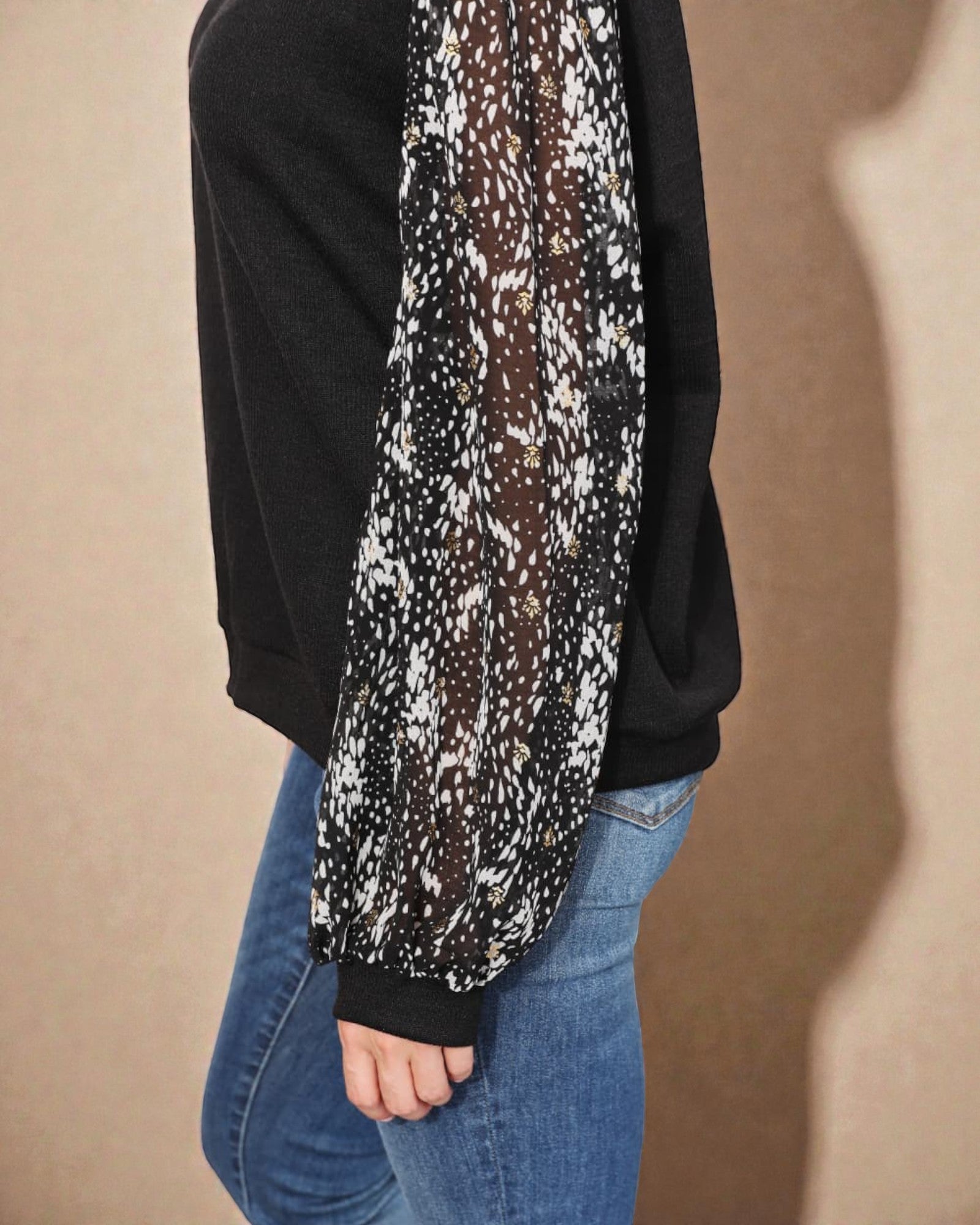 Person wearing a black sweater with a patterned long-sleeve shirt underneath, on a beige background