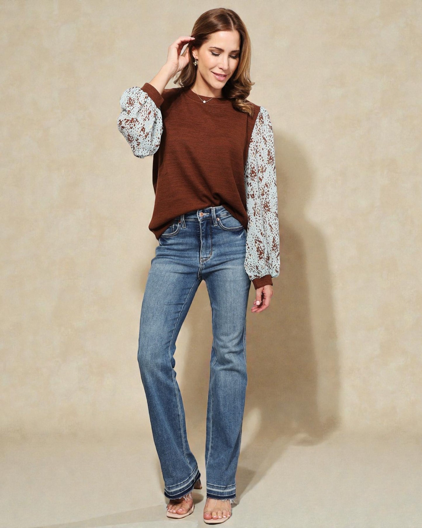 Woman wearing a brown top with floral sleeves and blue jeans against a beige background