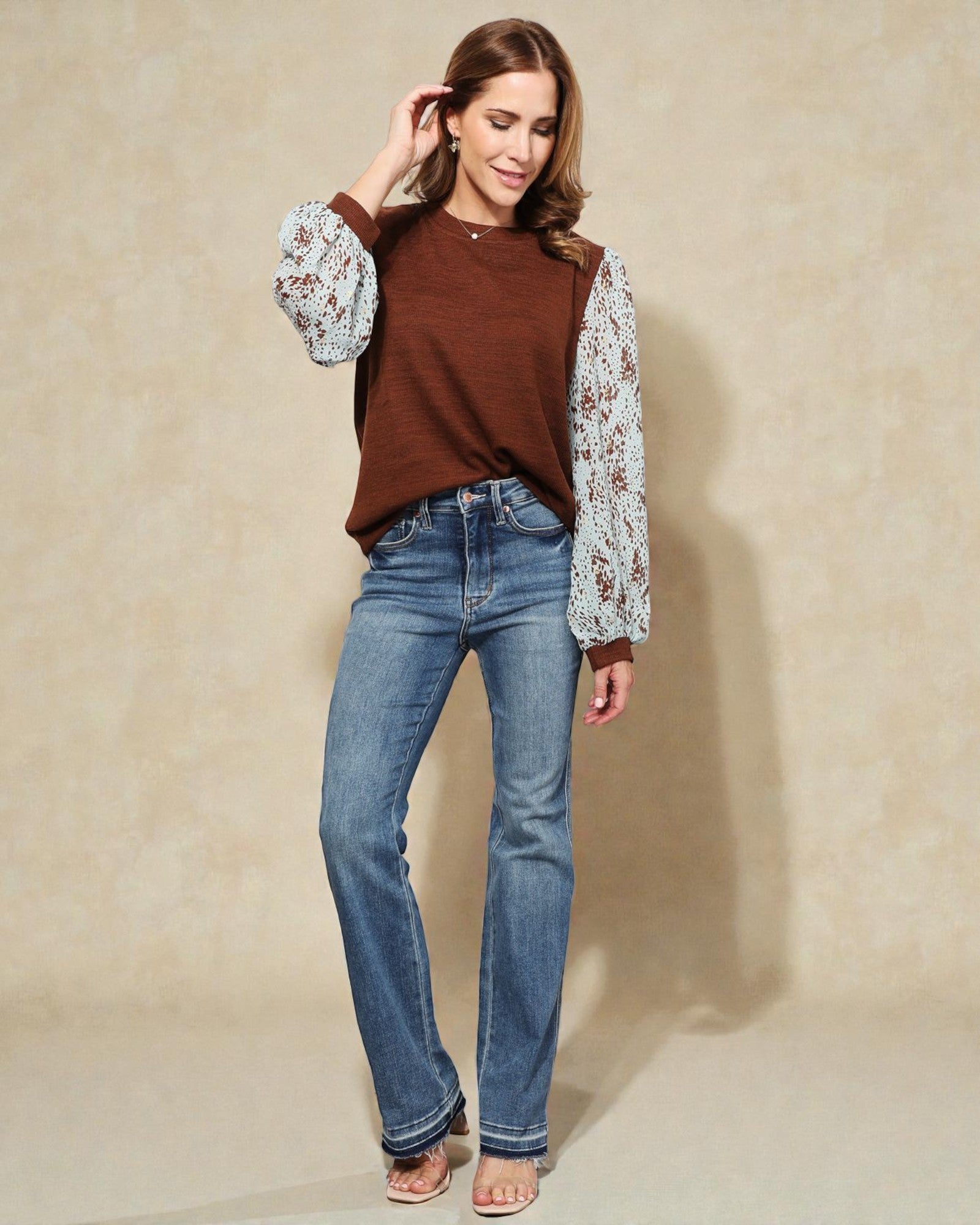 Woman wearing a brown top with floral sleeves and blue jeans against a beige background