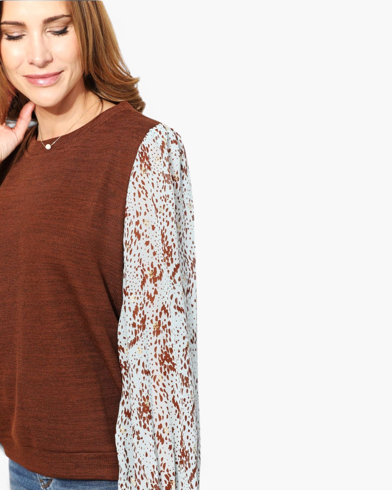 A woman wearing a brown knit top with one long sleeve in a brown and white leopard print pattern, shown against a plain white background.
