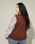 Woman wearing a brown sweater with floral sleeves against a beige background