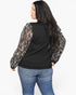 A woman shown from the back wearing a black long-sleeve top with sheer, sequined sleeves and blue jeans, against a plain white background.