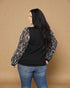 Person wearing a black top with sequin sleeves against a brown background